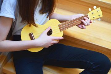Girl hands playing song on small yellow ukulele guitar. Music and hobbies concept.