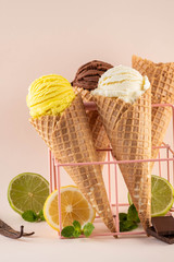 Assorted ice cream in sugar cones on pink background.