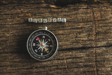 Fototapeta na wymiar Compass on wood deck with blocks of letters making the word survival.