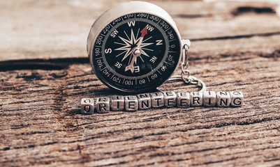 Compass on wood deck with blocks of letters making the word orienteering.