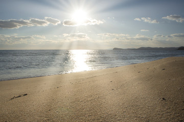 the Golden beach along the calm blue sea under a clear sky with white clouds and shining sun