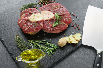 Raw Osso Buco steak on a black stone surrounded by spices