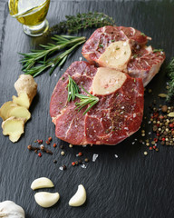 Raw Osso Buco steak on a black stone surrounded by spices