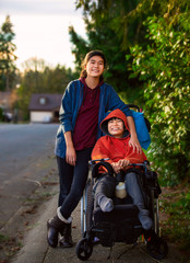 Sister standing next to disabled little brother in wheelchair outdoors