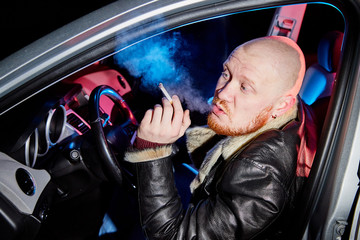 Male driver in a leather jacket smoking in the car in the dark. Night photo shoot