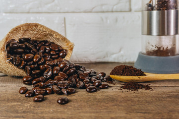 Roasted coffee beans in sacks and crushed coffee with a hand cranked coffee grinder were poured into a spoon on an old wooden table.