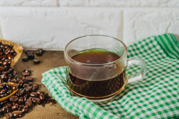 Roasted coffee beans in sacks and in spoons The clear glass that put the coffee water on the green and white cloth on the old wooden table