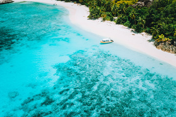 Aerial drone above view of paradise isolated beach. Lonely tourist boat in turquoise shallow lagoon ocean water surrounded by coconut trees