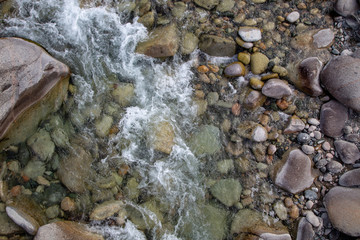 Water in the mountain raging river. Beautiful natural background of stones and water. Texture of clear water and fast river. Background to insert text. Tourism and travel.