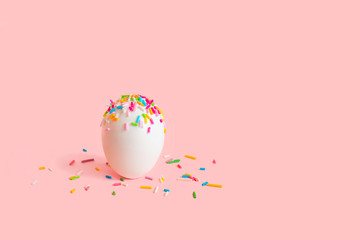 Easter egg decorated with sweet confectionery dressing on pink background. Minimal Easter concept.