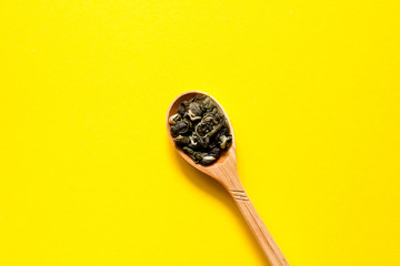 Biluochun. Chinese leaf green tea in a spoon on a yellow background. Top view and copy space.