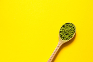 Matcha. Japanese powdered green tea in a spoon on a yellow background. Top view and copy space.