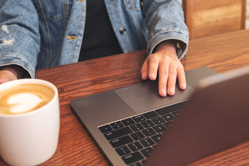 Closeup image of a woman using and touching on laptop touchpad on wooden table while drinking coffee