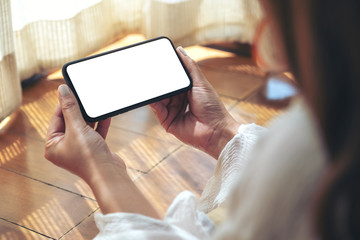 Mockup image of a woman holding and using black mobile phone with blank desktop screen horizontally while laying down on the floor with feeling relaxed