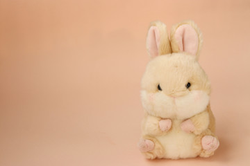 Soft toy rabbit on a peach background, free space for inscriptions