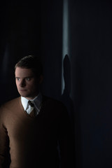 Fototapeta premium Man in white shirt and brown sweater in stripe of light.
