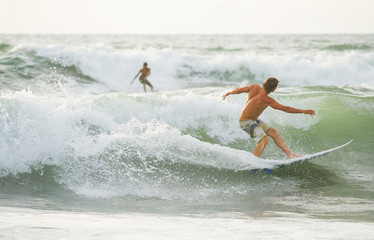 The surfer with tanned body  rolls on the waves at sunset.