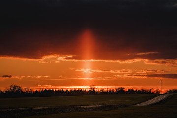 Sun pillar on the orange sunset cloudy sky.