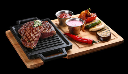 Fototapeta na wymiar Rib eye steak on wooden tray with grilled vegetables on dark background