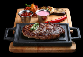 Rib eye steak on wooden tray with grilled vegetables on dark background