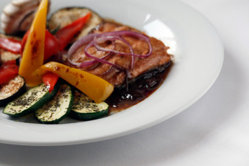 Grilled salmon fillet and grilled vegetables on a white porcelain plate.