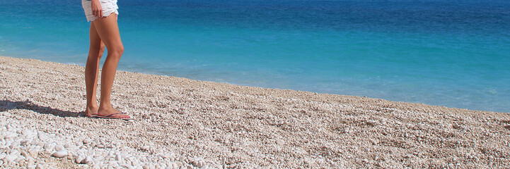 Fototapeta na wymiar Partial view on female legs on paradisiac white beach with turquoise water