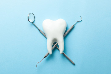 Tooth and dental instruments on blue background. Dental treatment. Dentist tools mirror, hook.