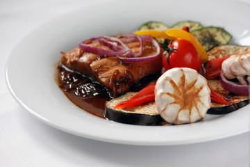 Grilled salmon fillet and grilled vegetables on a white porcelain plate.