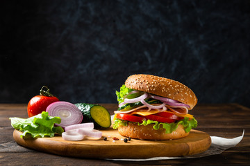 Sandwich burger with ham, cheese and vegetables on a wooden board with ingredients. Copy space. Fast food for breakfast or lunch. Concept for banner or advertisment
