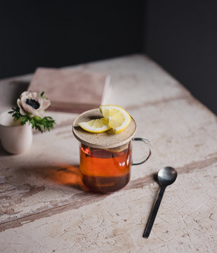 Tee mit Zitrone auf einem Tisch mit Blumen und kleinem Buch