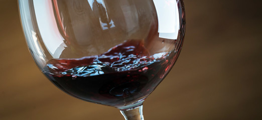Pouring red wine into the glass against wooden background
