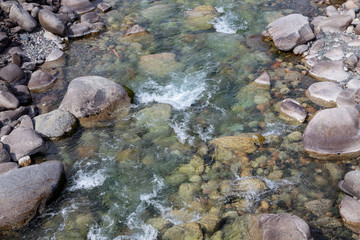 Fototapeta na wymiar Water in the mountain raging river. Beautiful natural background of stones and water. Texture of clear water and fast river. Background to insert text. Tourism and travel.