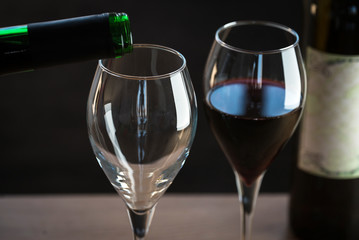 Pouring red wine into the glass against wooden background