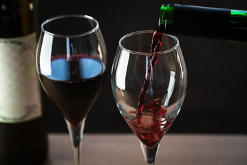 Pouring red wine into the glass against wooden background