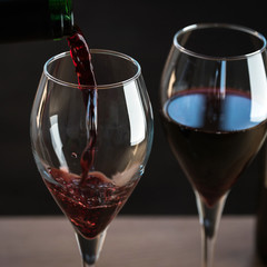 Pouring red wine into the glass against wooden background