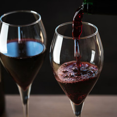 Pouring red wine into the glass against wooden background