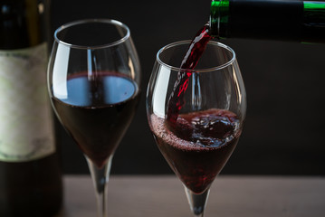 Pouring red wine into the glass against wooden background