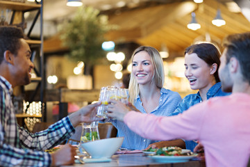 Happy four young friends toasting during festive dinner in restaurant