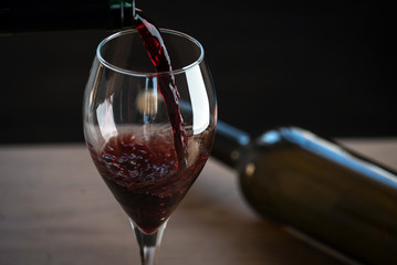 Pouring red wine into the glass against wooden background