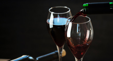 Pouring red wine into the glass against wooden background