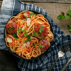 Spaghetti with meatballs, parmesan and tomato sauce in a bowl on a rustic wooden table. Tasty Italian pasta food. Top view shot.