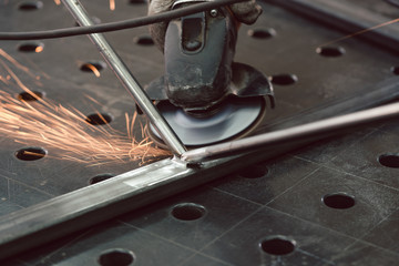 Worker in metal factory grinding workpiece with sparks flying