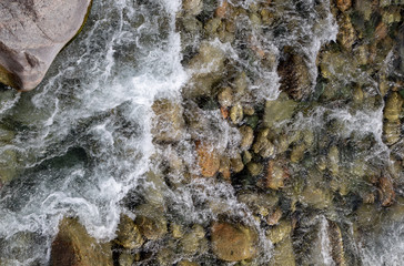 Water in the mountain raging river. Beautiful natural background of stones and water. Texture of clear water and fast river. Background to insert text. Tourism and travel.