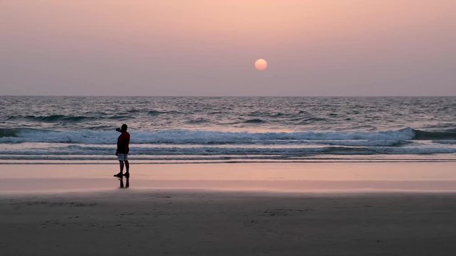 A man taking picture on the phone of dramatic sunset on the beach In India