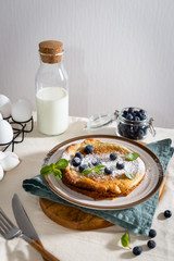 Homemade Dutch Baby Pancake with Blueberries, mint and Powdered Sugar. Delicious Pancake, blueberries, bottle of milk and eggs on the table. Served breakfast. Copy space