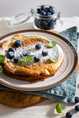 Fresh homemade Dutch Baby pancake with blueberries and mint on rustic linen background. Breakfast, restaurant, menu concept. Close up