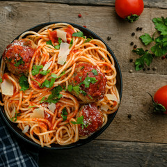 Traditional Italian spaghetti with meatballs and parmesan in tomato sauce in a black bowl. American family meal on a table. Top view shot.