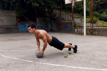 A fit, strong, muscular young man shirtless doing push up on a bascketball outside. Sport concept. © Dragosh