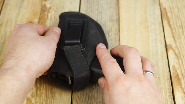 Human inserts a pistol into a holster and pulls it out of a holster on a wooden background.