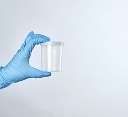 hand in a blue sterile glove holds a empty plastic container for collecting analyzes